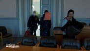In einem Gerichtssaal verdeckt eine angeklagte Frau ihr Gesicht mit einer roten Mappe. © NDR Foto: NDR Screenshot