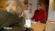 Ein Mann bedient eine Frau an einem Schalter eines Paketshops. © NDR Foto: NDR Screenshot