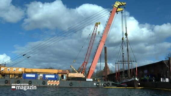 Ein aus dem Wasser geborgenes Schiff hängt an gurten eines Schwimmkrans © NDR Foto: NDR Screenshot