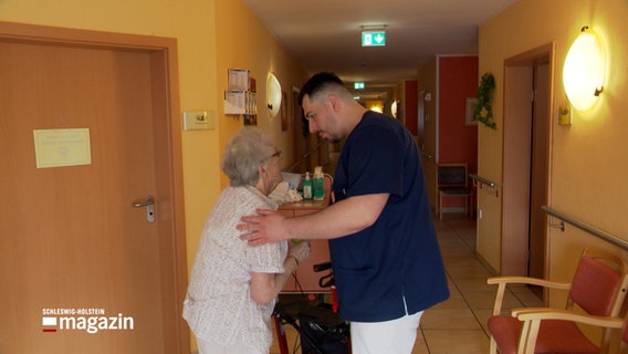 Ein Mann in einem blauen Arztkittel spricht mit einer Seniorin © NDR Foto: NDR Screenshot
