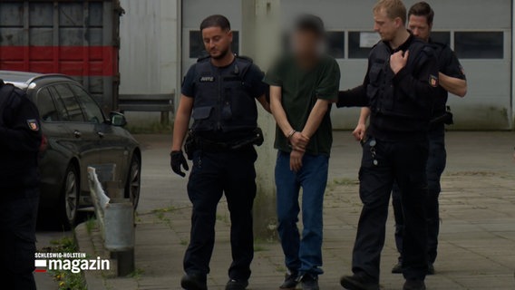 Eine unkenntlich gemachte Person wird von Polizisten in handschellen abgeführt © NDR Foto: NDR Screenshot