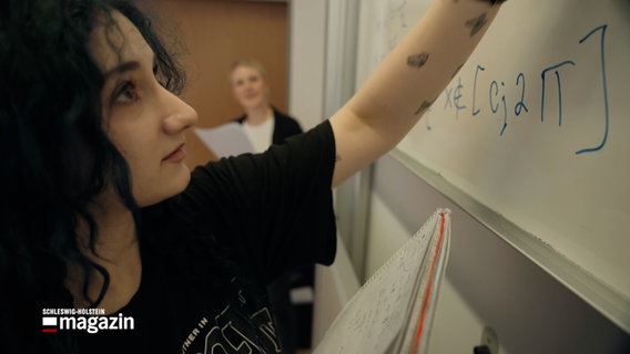 Eine junge Frau schreibt mit einem Marker an eine Tafel © NDR Foto: NDR Screenshot