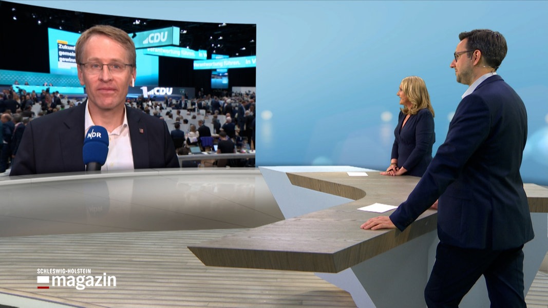 Die NDR-Moderatoren Harriet Heise und Christopher Scheffelmeier stehen im NDR Schleswig-Holstein Studio während Miniterpräsident Daniel Günther per Video zugeschaltet ist und ein interview gibt.