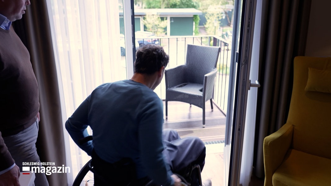 Ein Mann in einem Rollstuhl fährt auf einen Balkon eines Hotelzimmers