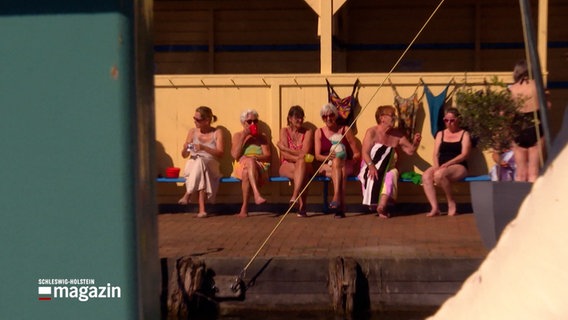 Mehrere Frauen in Badeanzügen sitzen auf einer Bank in einem Freibad © NDR Foto: NDR Screenshot