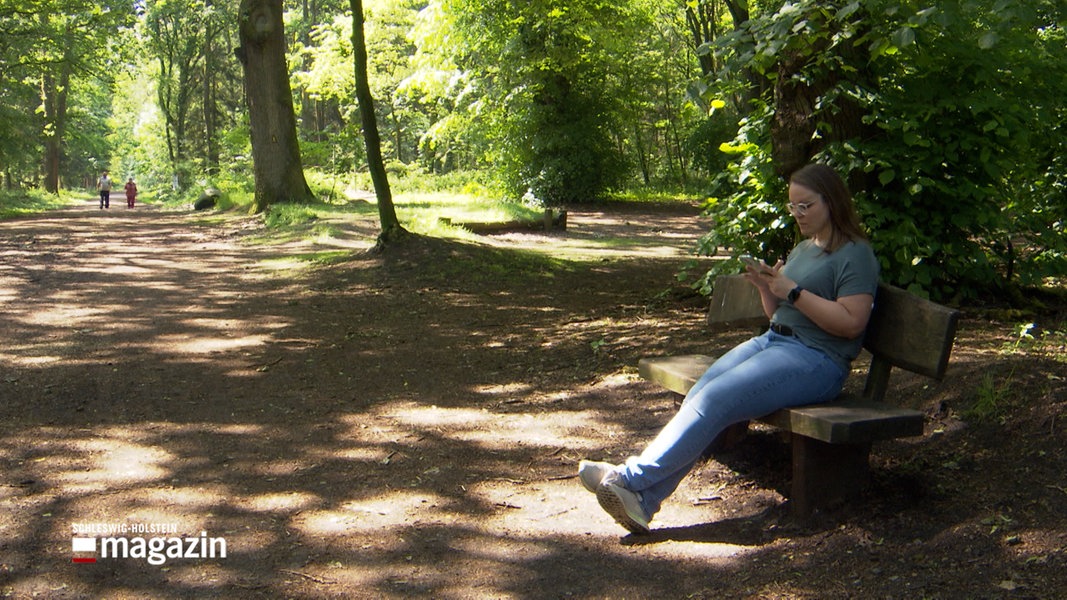 Eine Frau sitzt auf einer Bank in einem Wald und schaut auf ihr Smartphone