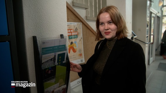 Eine Junge Frau steht vor einem Plakat © NDR Foto: NDR Screenshot