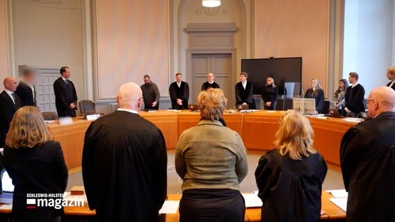 Menschen stehen bei einem Prozessginn im Gerichtssaal © NDR Screenshot 