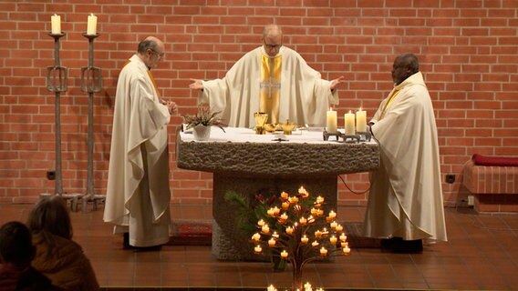 Drei katholische Pfarrer stehen bei einer Profanierung in einer Kirche © NDR Screenshot 