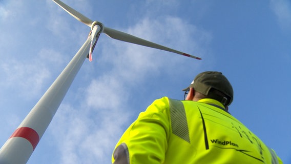 Matthias Frauen steht in einem Windpark vor einer neuen Windkraftanlage und guckt hoch © NDR Screenshot 