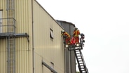 Feuerwehr steht mit Leiter am Fenster einer rauchenden Trocknungsanlage eines Silos in Neumünster. © Digitalfotografie Nyfeler & Jappe Foto: Maria Nyfeler