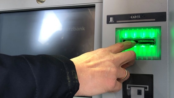 Eine Polizistin zeigt mit dem Zeigefinger auf eine manipulierte Karten-Vorrichtung an einem Geldautomaten. © NDR Foto: Julia Jänisch