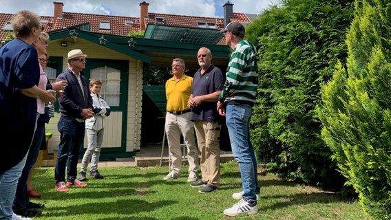 Eine Gruppe von Leuten stehen in einem Garten, neben einem Solar-Panel. © NDR Foto: Lena Haamann