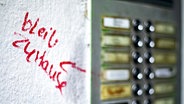 Neben einer Klingelleiste steht mit rotem Marker auf die weiße Wand geschrieben: "Blieb zu Hause" © Imago Images Foto: photothek