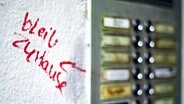 Neben einer Klingelleiste steht mit rotem Marker auf die weiße Wand geschrieben: "Bleib zu Hause" © Imago Images Foto: photothek