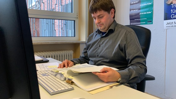 Ein Mann sitzt in einem Büro an einem Arbeitstisch mit einem PC-Monitor. Ein Mann sitzt in einem Büro an einem Arbeitstisch mit einem PC-Monitor. © NDR Foto: Corinna Below