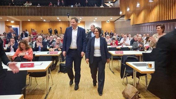 Serpil Midyatli (r.) und Lars Klingbeil (l.) gehen zusammen durch einen großen Konferenzraum bei dem SPD-Parteitag. Serpil Midyatli (r.) und Lars Klingbeil (l.) gehen zusammen durch einen großen Konferenzraum bei dem SPD-Parteitag. © NDR Foto: Sylvia Aust