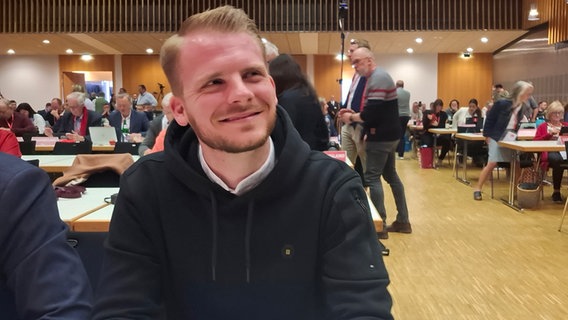 Tim Klüssendorf, SPD-Bundestagsabgeordneter, sitzt an einem Tisch in einem großen Konferenzraum bei dem SPD-Parteitag. Tim Klüssendorf, SPD-Bundestagsabgeordneter, sitzt an einem Tisch in einem großen Konferenzraum bei dem SPD-Parteitag. © NDR Foto: Sylvia Aust