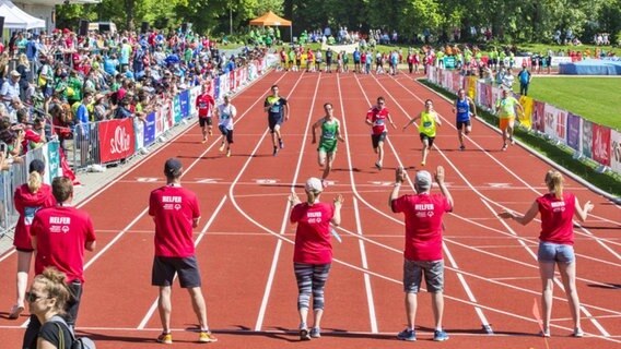 In einem Stadion sprinten Sportler auf der Laufbahn Helfern entgegen. Auf den Stadionrängen sitzen Zuschauer. © SOD Foto: Florian Conrads