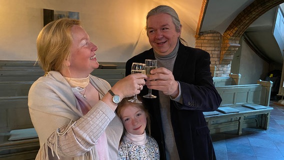 Ein Hochzeitspaar stößt mit Kind im Arm mit einem Glas Sekt nach der Trauung in der Kirche an © NDR Foto: Lisa Knittel