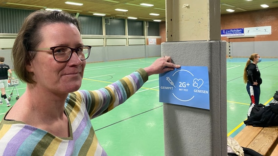 Eine Frau bringt einen Hygiene-Hinweis in einer Sporthalle an einen Pfeiler an. © NDR Foto: Andrea Schmidt