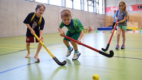 Zwei Jungen und ein Mädchen spielen Hockey in einer Sporthalle. © picture alliance / Pressefoto ULMER Foto: Markus Ulmer