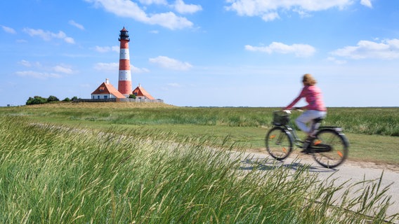 Eine Radfahrerin befährt einen kleinen Weg zu einem Leuchtturm. © RAD.SH 
