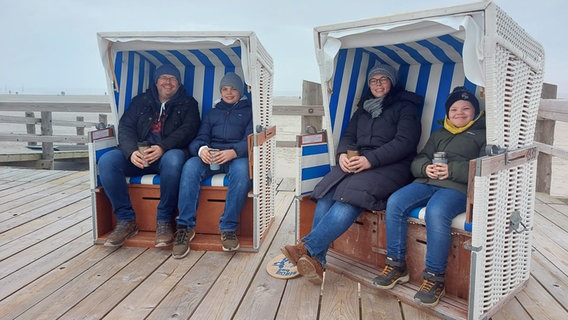Czteroosobowa rodzina siedzi na dwóch leżakach na plaży w St. Peter-Ording.  © NDR Zdjęcie: Laura Albus