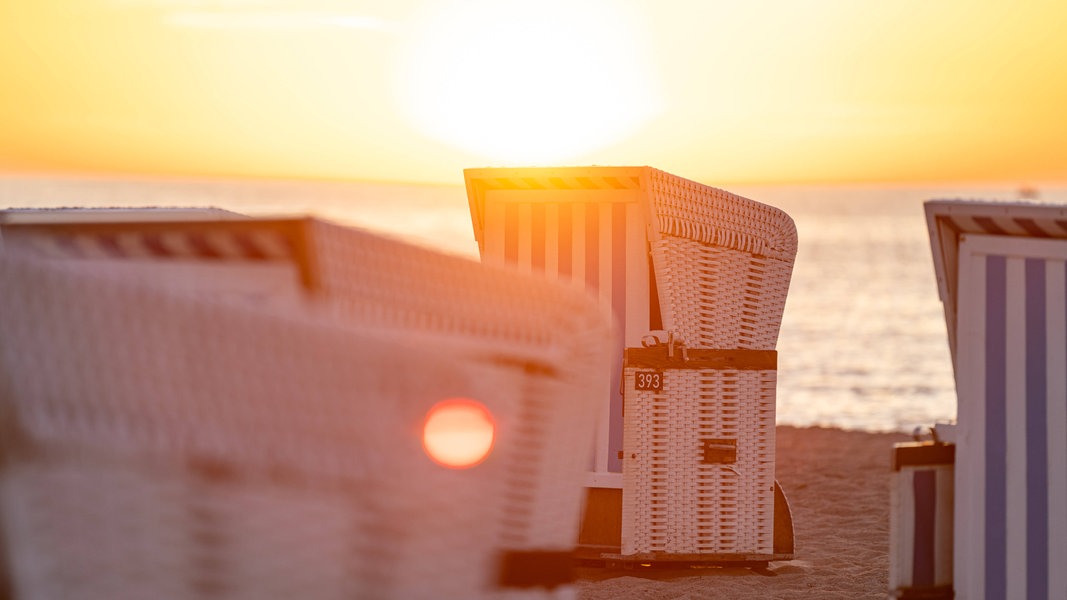 Strandkörbe am Strand bei untergehender Sonne.