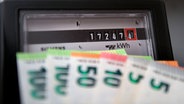 Euro-Geldschein werden vor einem Stromzähler im Privathaushalt gehalten. © IMAGO / MiS 