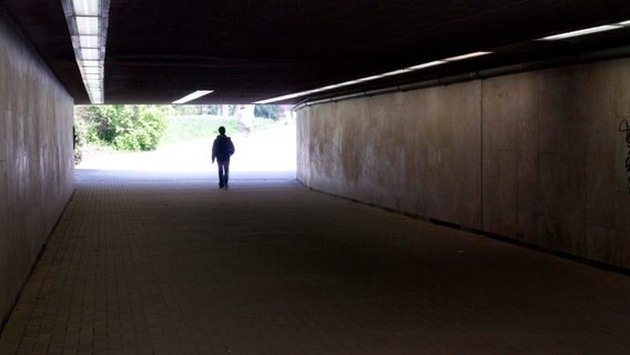 Ein junger Mann geht durch eine dunkle Unterführung. © picture alliance / imageBROKER | Movementway 