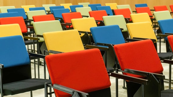 Mehrere Stühle in verschiedenen Farben stehen leer in einem Saal. © IMAGO / Cavan Images 