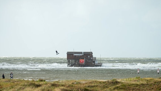 Ein Kiter fliegt über das Wasser auf dem überfluteten Strand von St. Peter Ording. © Jonas Walzberg/dpa Foto: Jonas Walzberg