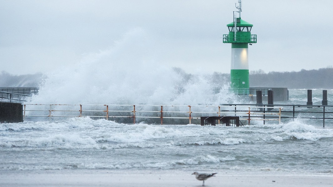 Wellen schlagen während eines Sturms am Strand an der Ostsee an einem Leuchtturm an der Einfahrt zur Trave hoch.
