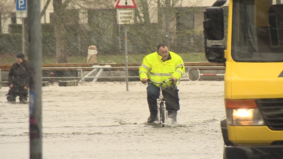 Ein Mann kämpft sich mit einem Fahrrad durchs Hochwasser in Lübeck.