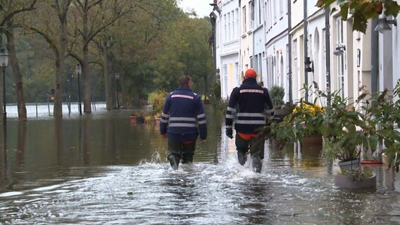 Zwei Männer in Anglerhosen laufen über eine überflutete Straße. © TNN 