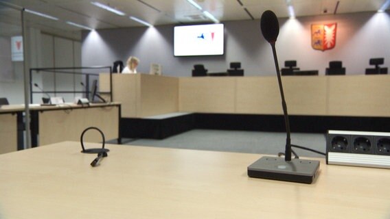 Ein Mikrofon steht auf einem Tisch in einem Prozesssaal © NDR Foto: NDR Screenshot