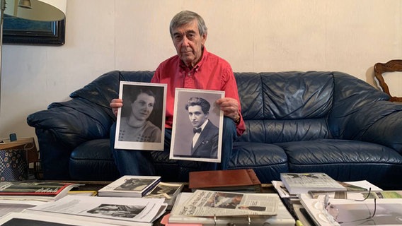Josef Salomonovic sitzend auf auf dem Sofa in den Händen Fotos von seiner Mutter und seinem Vater. © NDR Foto: Corinna Below