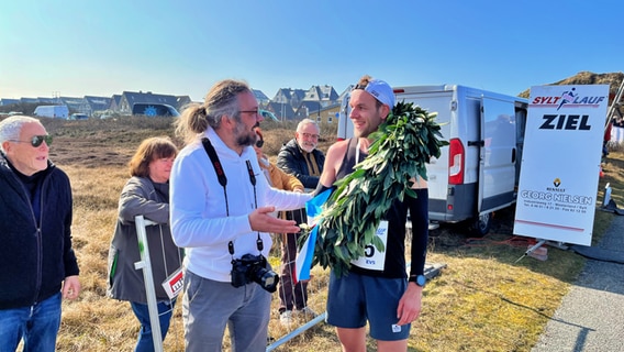 Der Sieger des Syltlaufes 2023 Christian Exner nach dem Zieleinlauf und mit einem Siegerkranz © Lars Grüning/NDR Foto: Lars Grüning