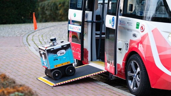 Ein kleiner Roboter fährt über eine Rampe in einen Bus.  Foto: TUHH/Marko Thiel