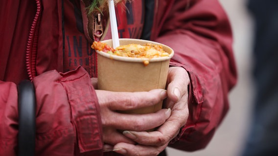 Ein Frau hält einen Becker mit einer Mahlzeit in der Hand. © picture alliance / dpa Foto: Oliver Berg