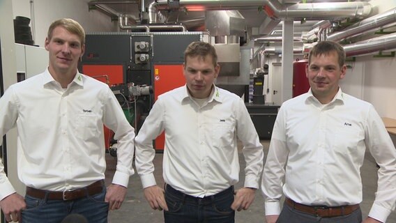 Drei Männer in weißen Hemden stehen in einer Maschinenhalle. © NDR 
