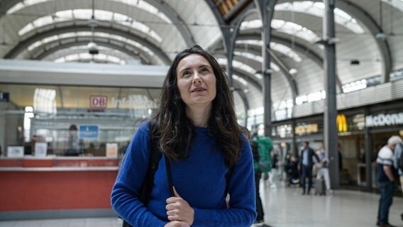 Reporterin Lisa schaut in der Kieler Bahnhofshalle hoch auf die Anzeigetafel. © NDR Foto: Dominik Dührsen