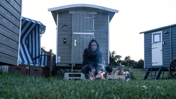 Reporterin Lisa sitzt an einem kleinen Holzfeuer vor ihrem Strandwagen. © NDR Foto: Dominik Dührsen