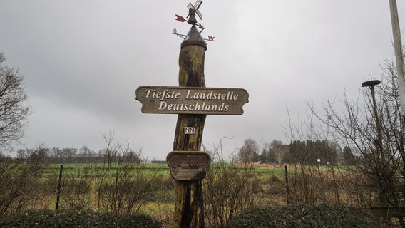 An einem Pfahl in einer ländlichen Gegend hängt ein Schild mit der Aufschrift "Tiefste Landstelle Deutschlands". © NDR Foto: Lisa Pandelaki