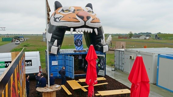 Hinter Bierbänken ragt ist großer, aufgeblasener Tigerkopf aus Plastikfolie auf. © NDR Foto: Peer-Axel Kroeske