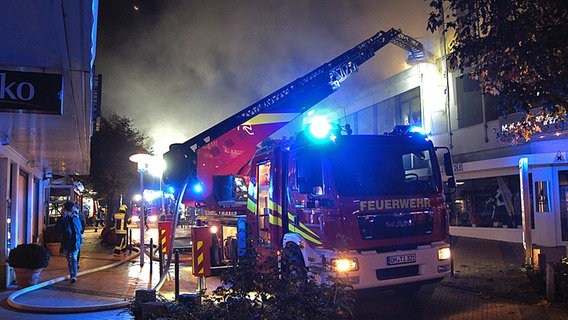Ein Wagen der Feuerwehr steht vor einem brennenden Gebäude © NDR Foto: Julian Marxen