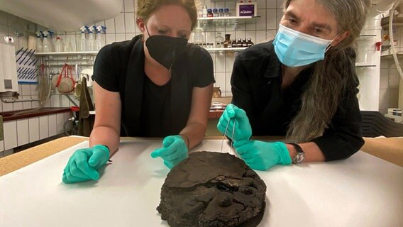 Lisa Renn (links) und Doris Mührenberg von der Lübecker Archäologie inspizieren eine beim Luftangriff 1942 verschüttete Torte. © Hansestadt Lübeck 
