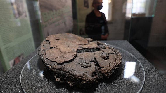 Eine verkohlte Torte liegt in einer Vitrine bei einem Pressetermin zur Ausstellung "Bittersüß - Der Tortenfund von Lübeck· im Museum Holstentor. © dpa-Bildfunk Foto: Christian Charisius