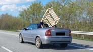 Ein Autofahrer transportiert ein großes Holzregal während der Fahrt in seinem Cabrio. © Presseportal Foto: Polizeidirektion Neumünster
